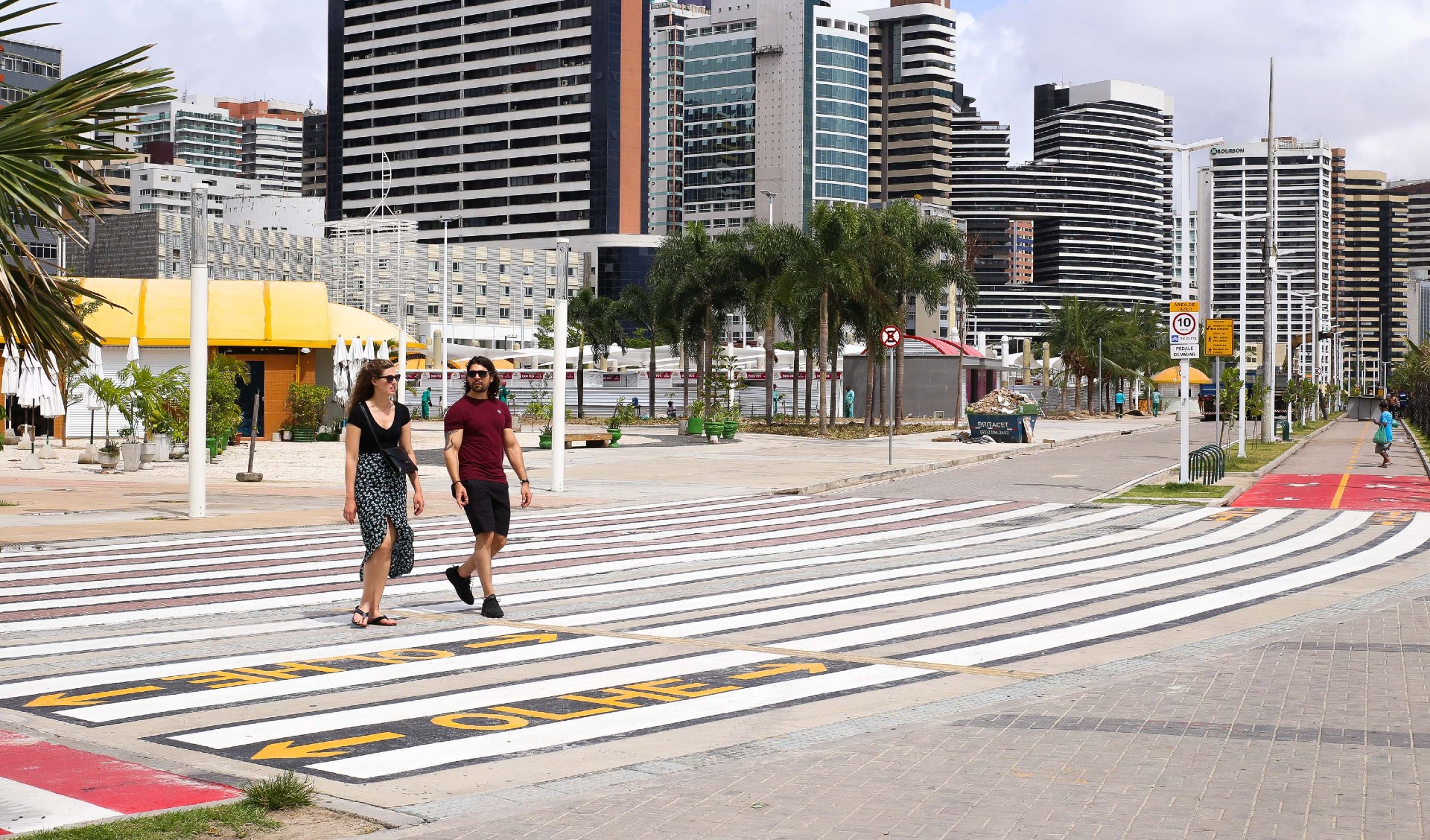 um homem e uma mulher atravessando a faixa de pedestres na beira-mar
